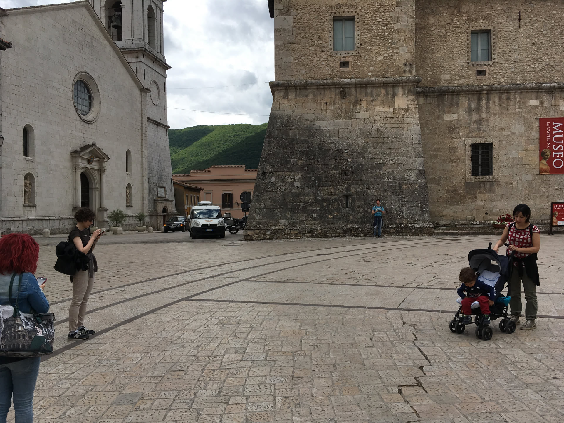 Piazza San Benedetto a Norcia nel giugno 2016: a sinistra la basilica intatta con il campanile, a destra il bastione della Castellina, alcune persone in piazza