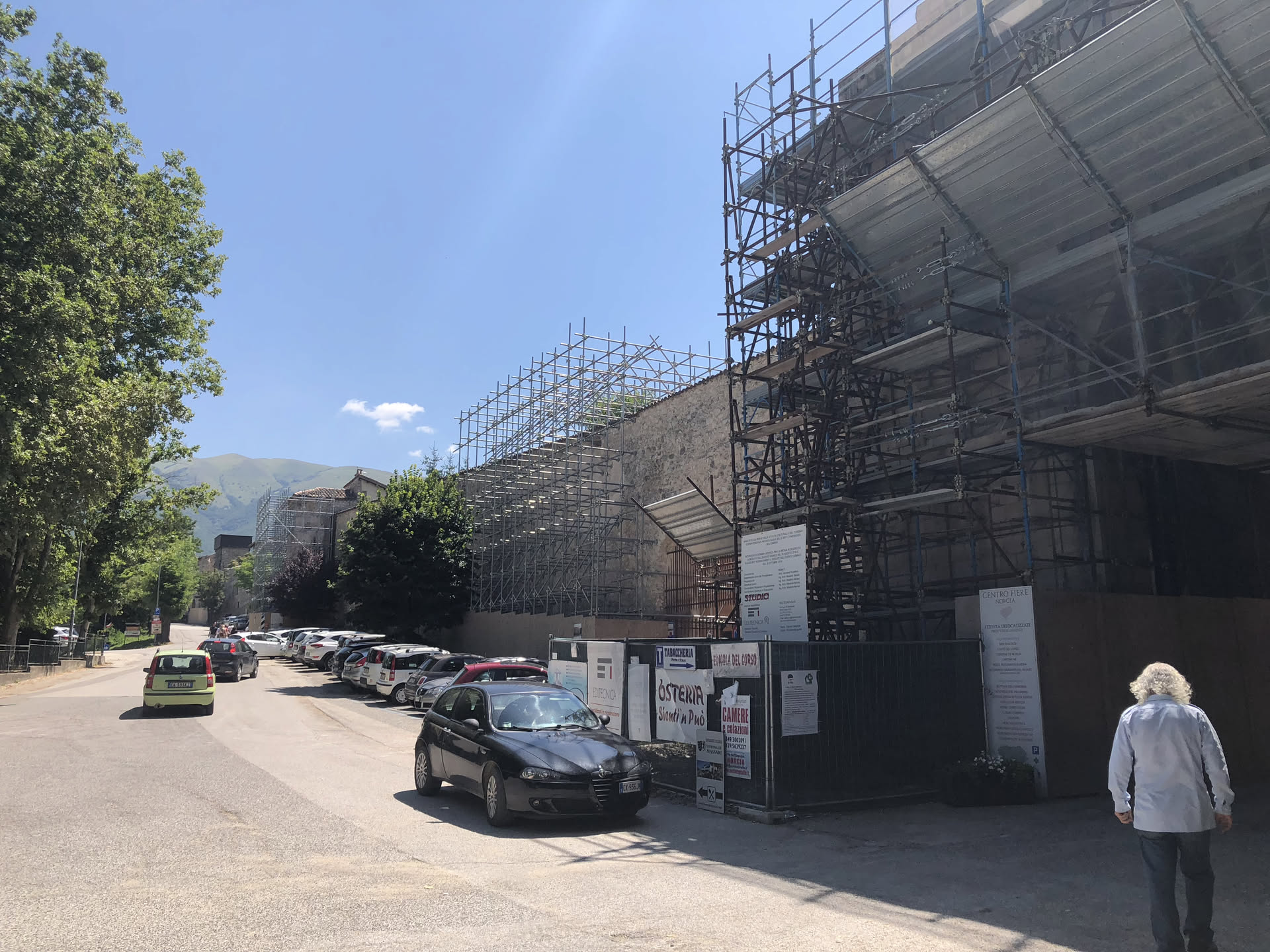 Norcia nel 2018: ponteggi e puntelli che corrono lungo un intero fronte di edifici, recinzioni di cantiere e auto parcheggiate lungo la strada