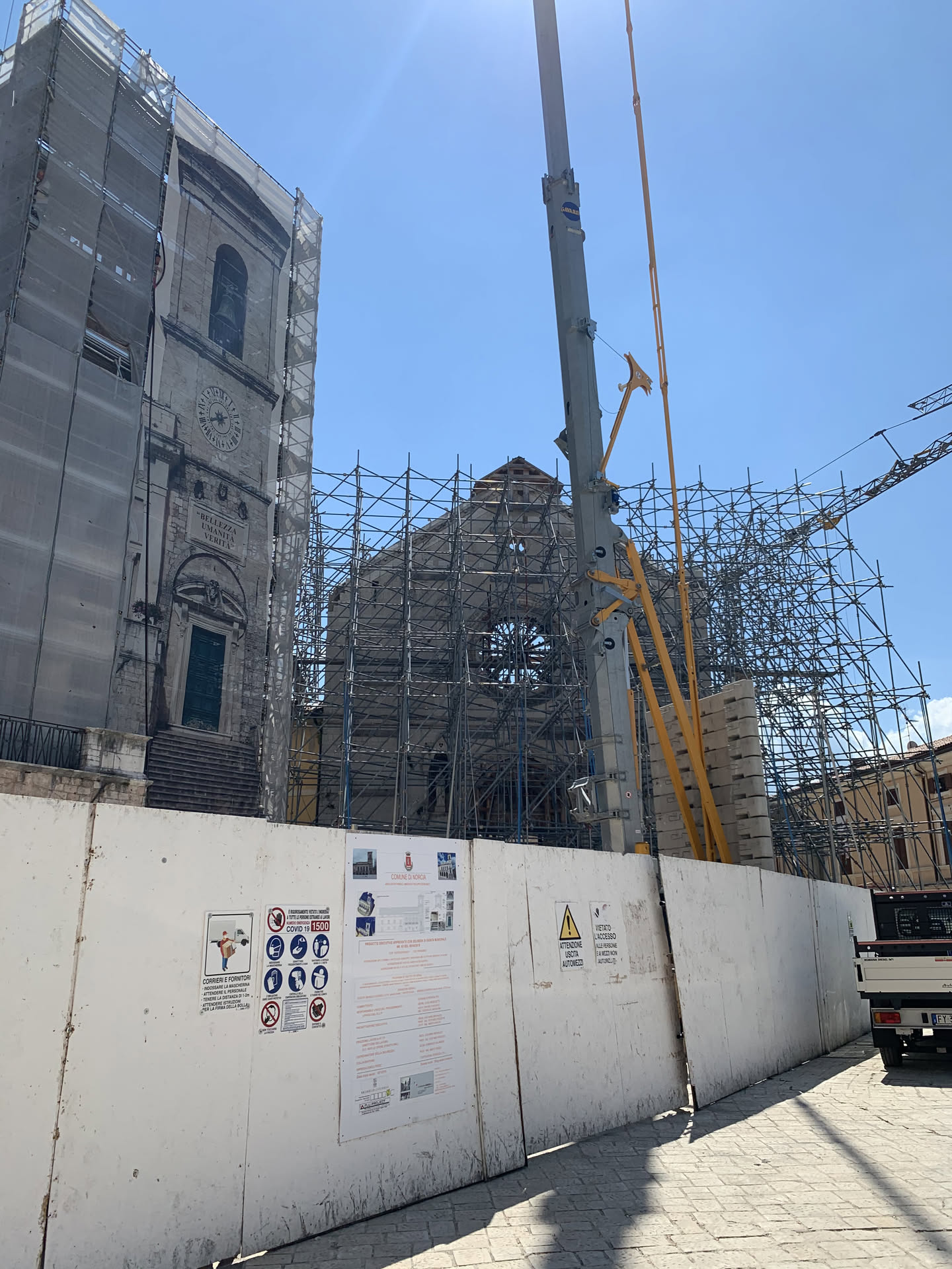 Il campanile della basilica avvolto nella rete con la scritta «Bellezza Umanità Verità» sulla facciata, e dietro il timpano superstite dentro una gabbia di tubi