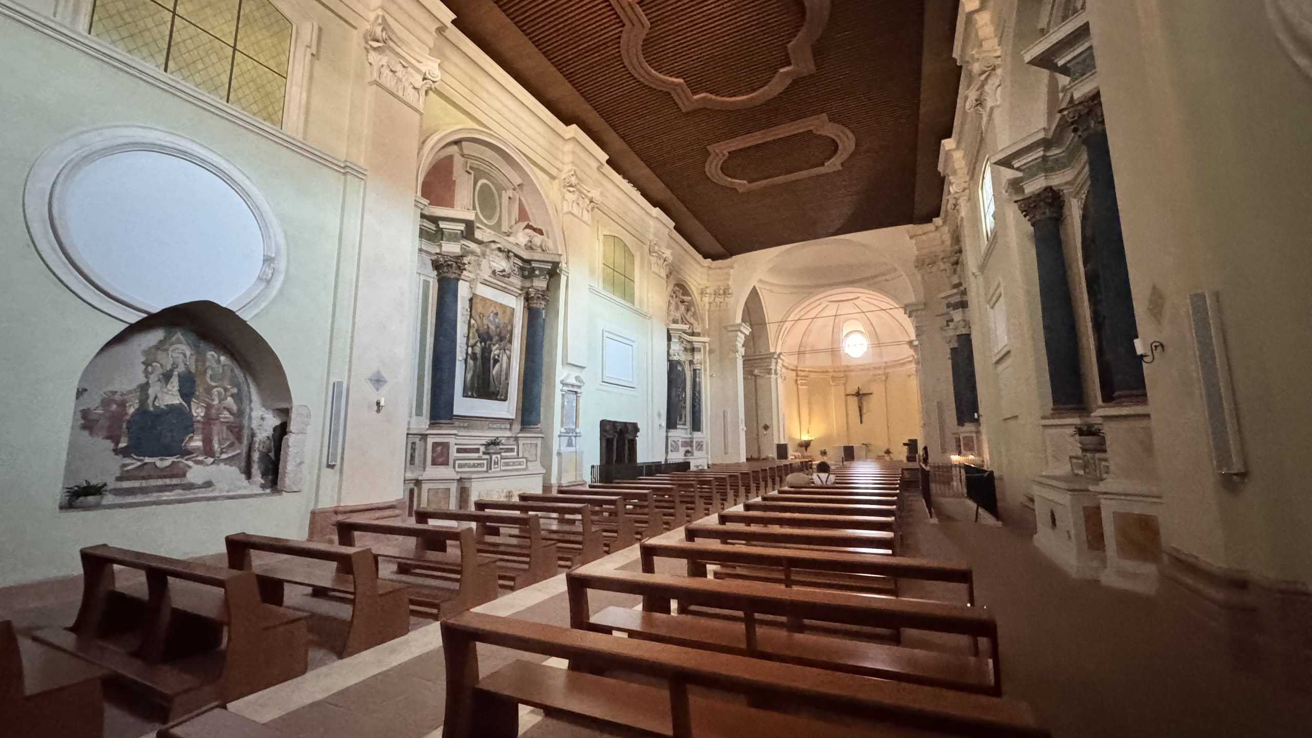 La navata della basilica riaperta nel 2026: banchi nuovi in fila, altari laterali con colonne blu, soffitto a cassettoni e in fondo il catino absidale con il crocifisso