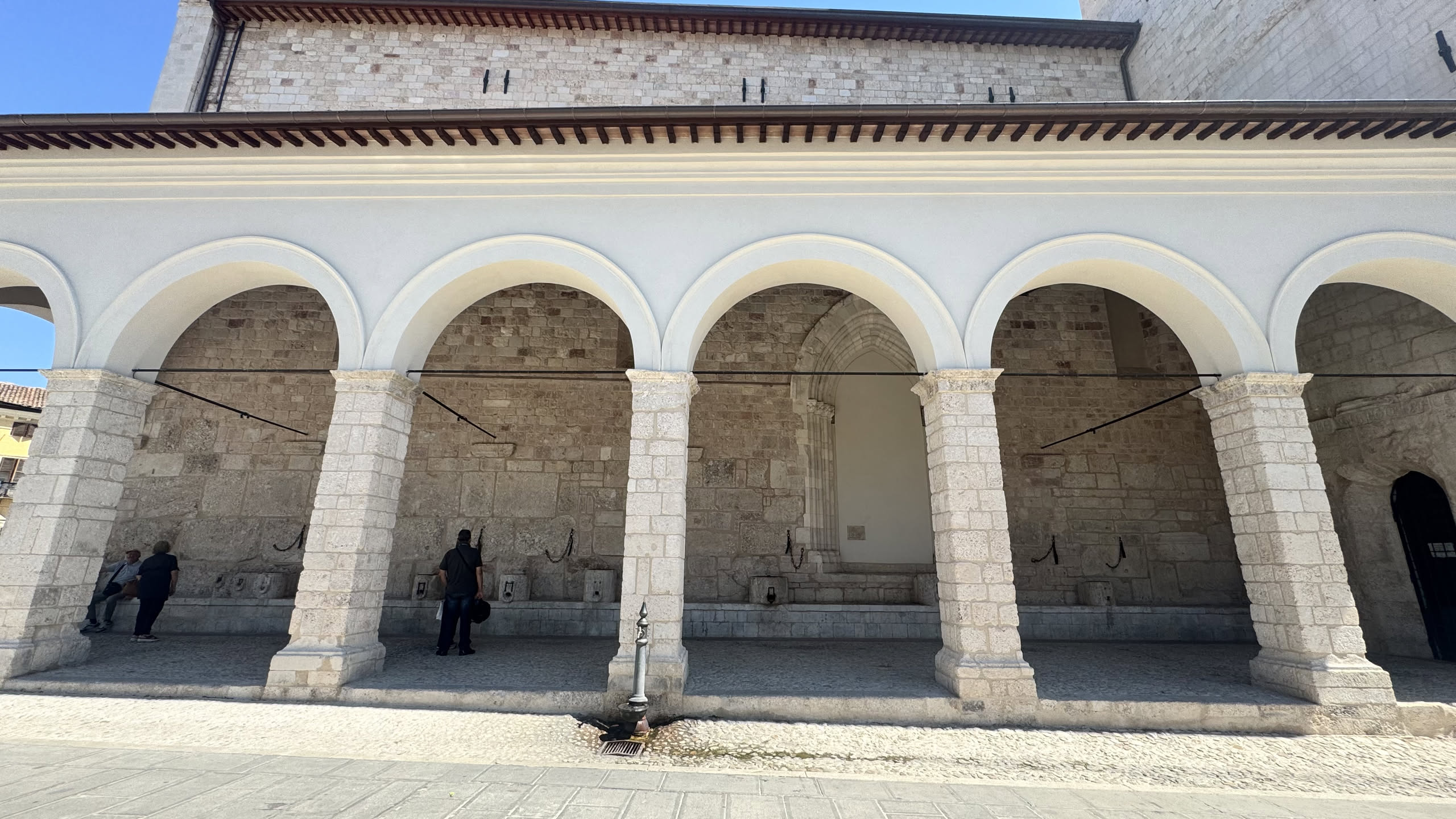 Il Portico delle Misure restaurato: arcate bianche su pilastri di pietra e, lungo il muro, i blocchi con le cavità usate per misurare i cereali