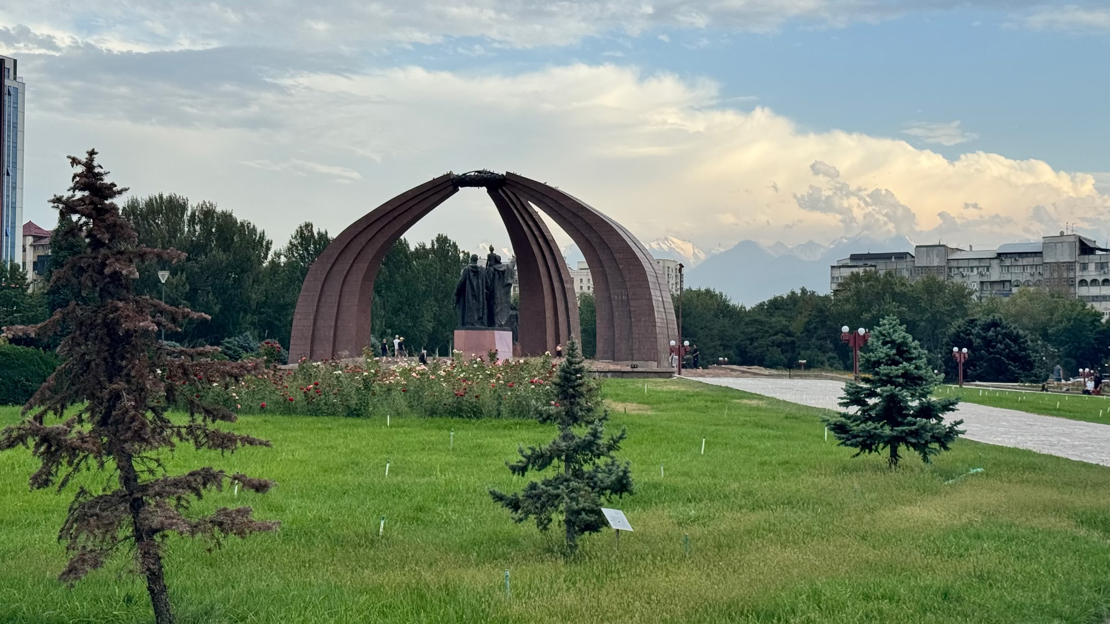 Il Monumento alla Vittoria: tre archi di granito a forma di pali di yurta in mezzo al prato, con le montagne all'orizzonte
