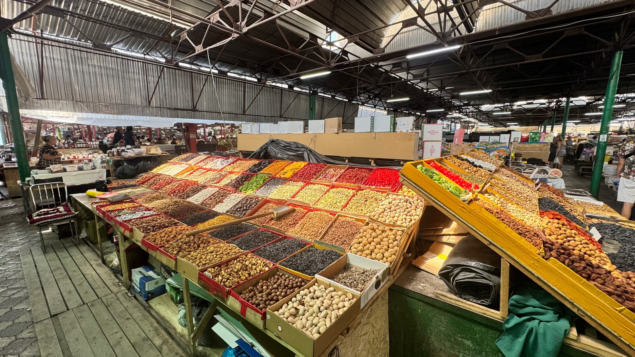 Una navata dell'Osh Bazar: banchi lunghissimi coperti di frutta secca, noci e spezie sotto il tetto di lamiera