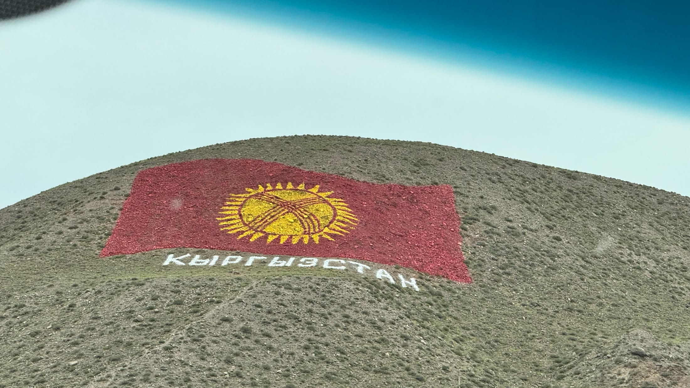 La bandiera del Kirghizistan disegnata a terra su una collina spelacchiata, con la scritta КЫРГЫЗСТАН sotto il sole rosso e giallo