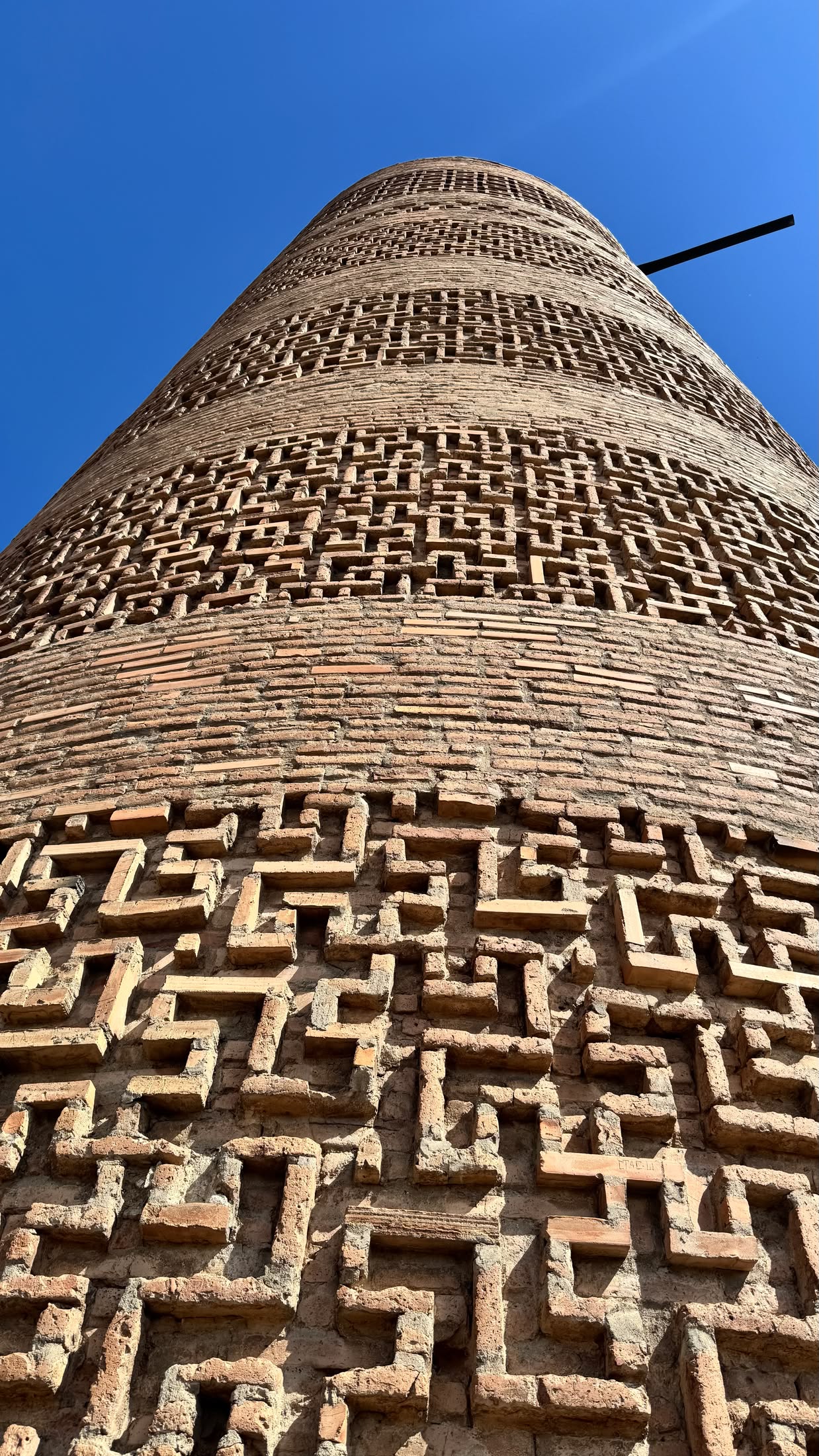 Dettaglio della muratura della torre ripresa dal basso: fasce di mattoni disposti a motivi geometrici contro il cielo blu
