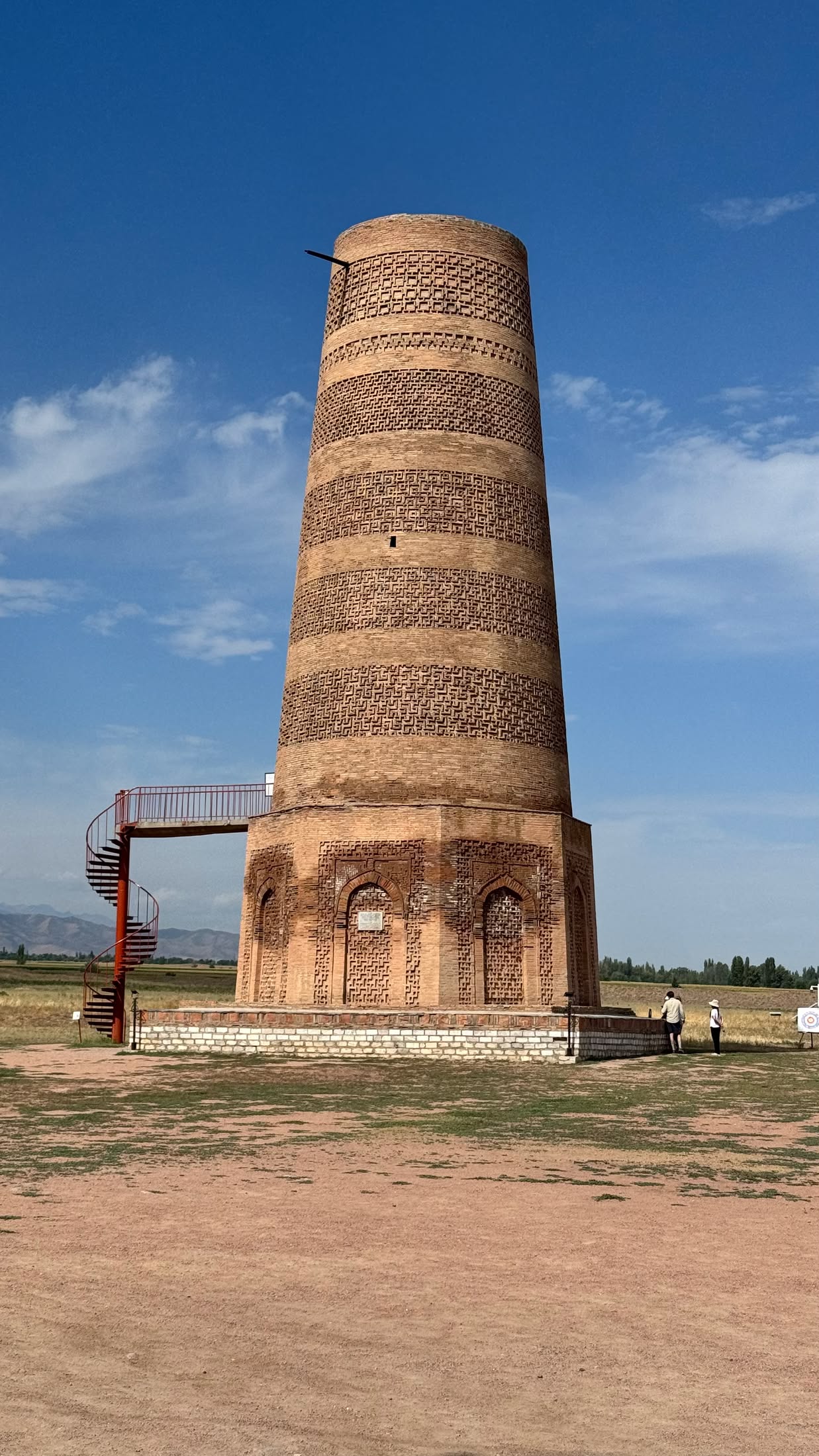 Il minareto di Burana visto da vicino: mattoni a fasce decorate e la scala di ferro rossa che porta all'ingresso rialzato