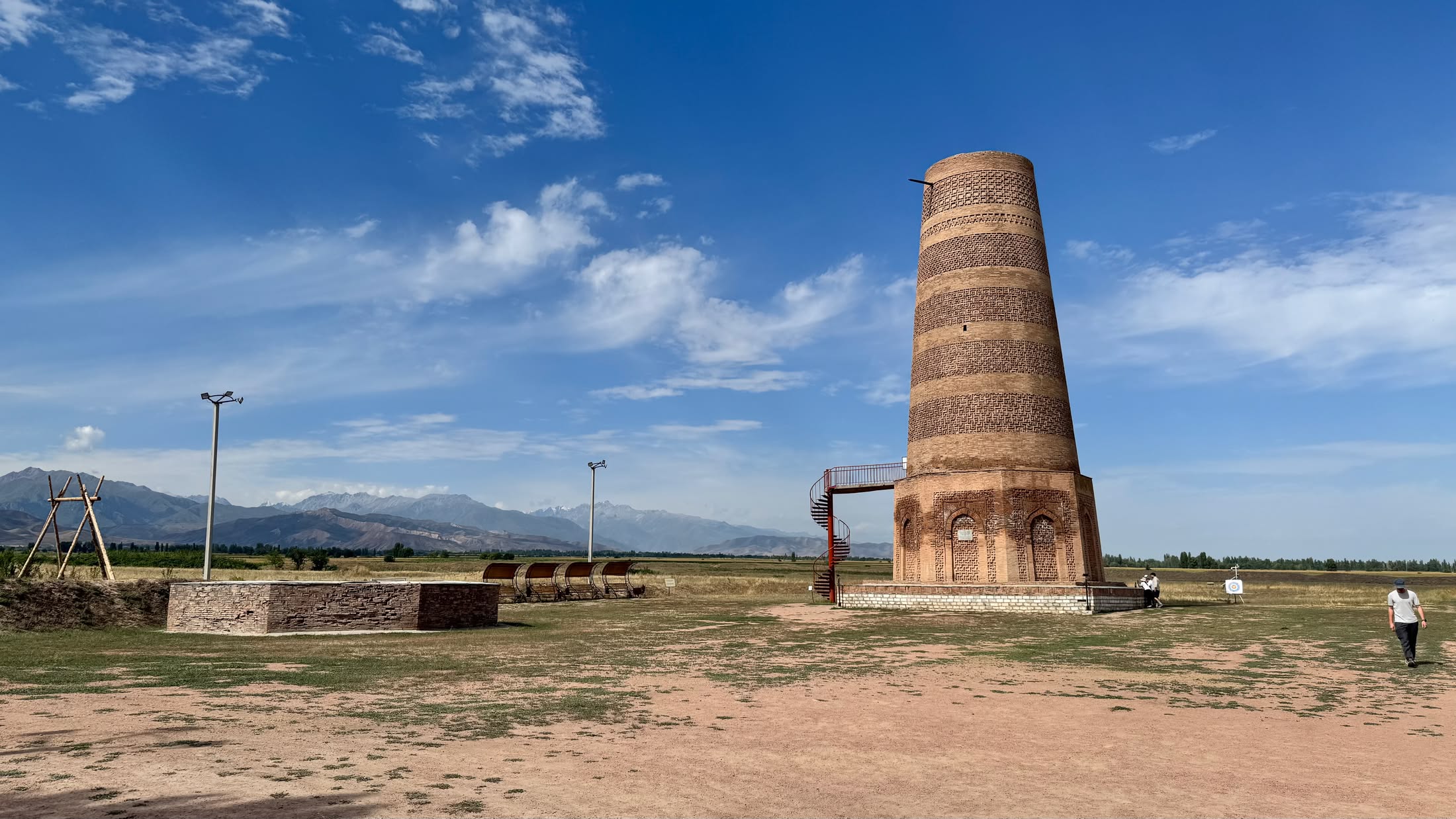 La torre di Burana nella piana secca, con la catena del Kirghizistan innevata all'orizzonte e nuvole alte sul cielo blu