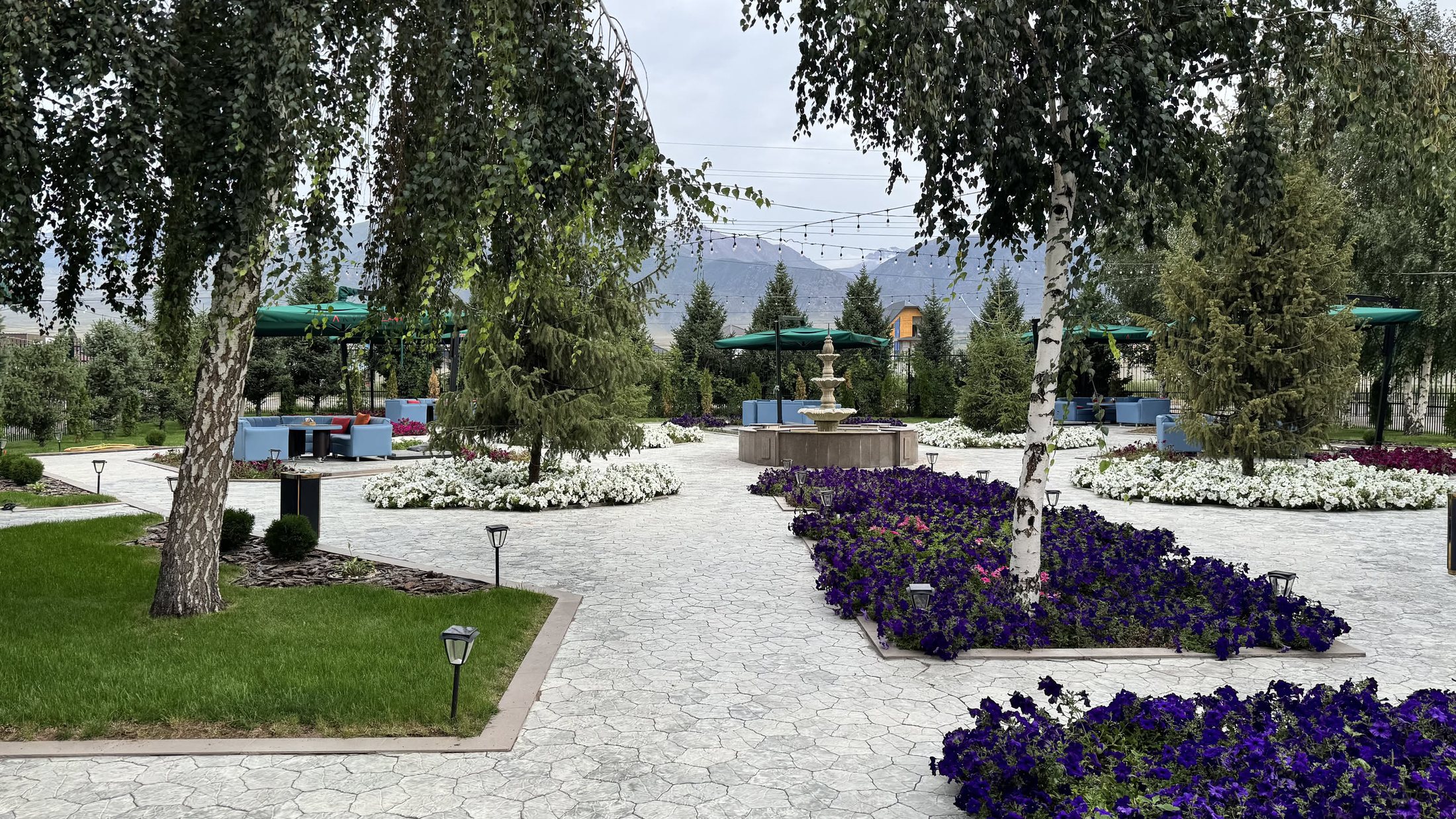 Il giardino del resort la mattina: aiuole di fiori viola disegnate a mano, ghiaia bianca, gazebo e il lago che si intravede in fondo