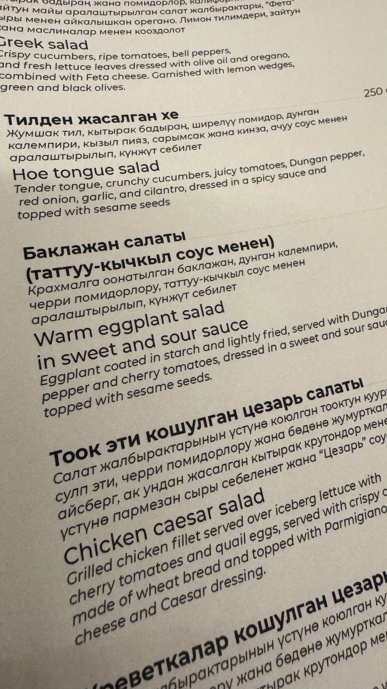 La pagina del menù in kirghiso e inglese, con la «Hoe tongue salad» e l'insalata tiepida di melanzane in agrodolce