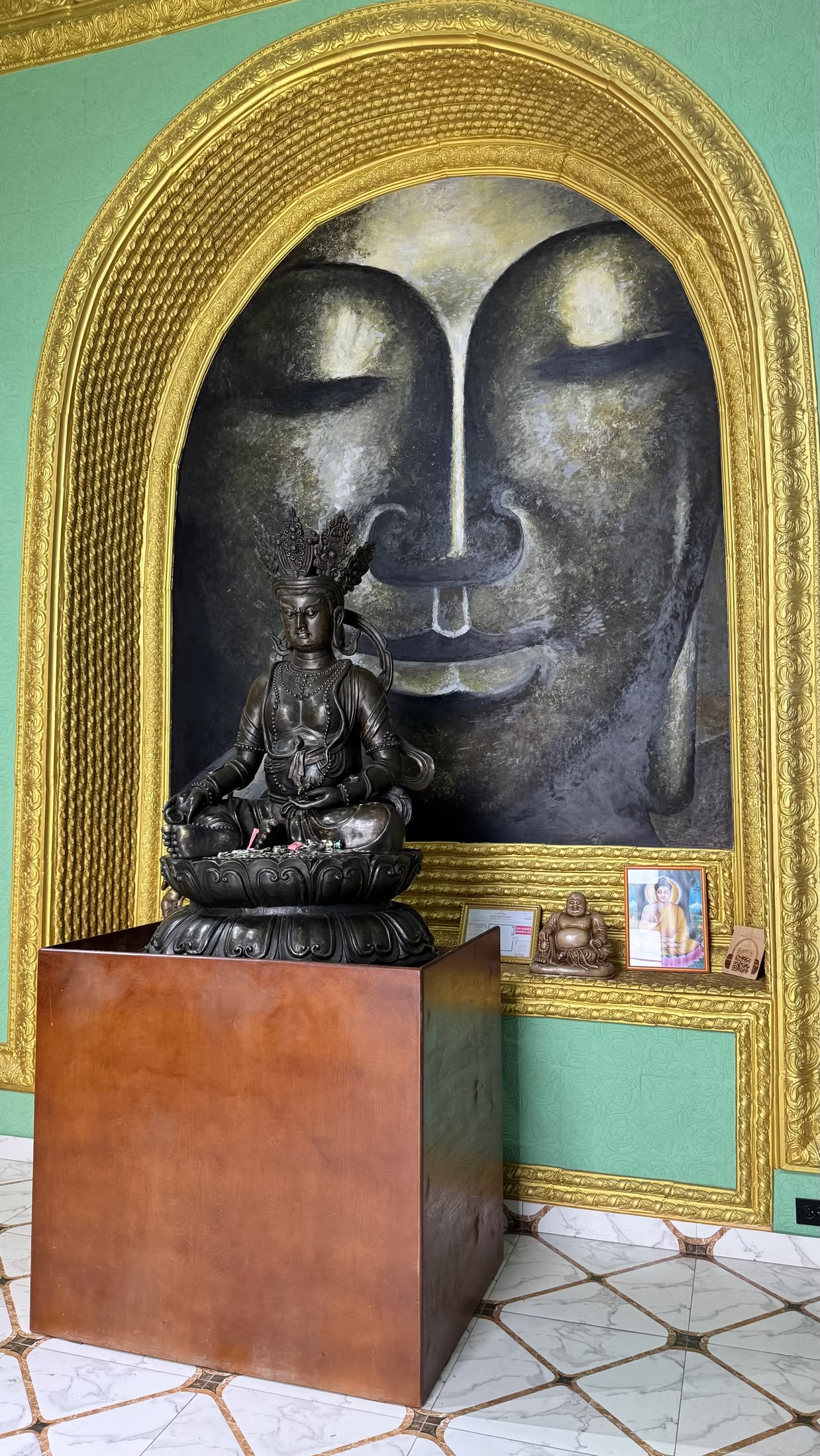 Una statua dorata in una nicchia di Rukh Ordo, davanti a un grande volto di Buddha dipinto sulla parete verde
