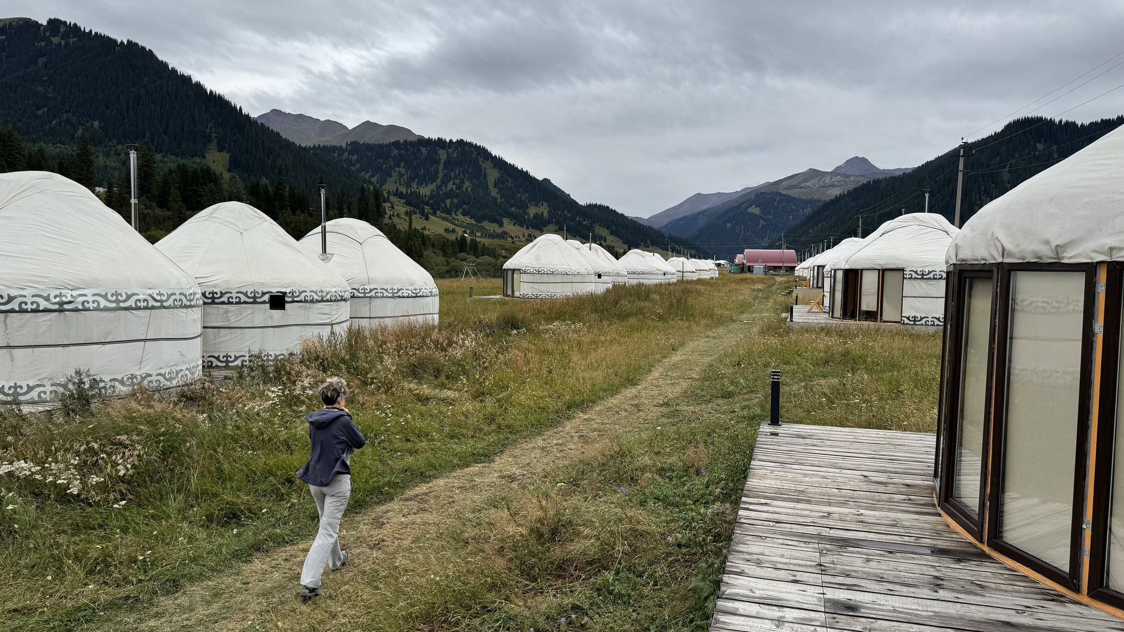 Le yurte in fila sul prato del campo Ak-Sai, unite dalle passerelle di legno, con le nuvole basse sulle creste
