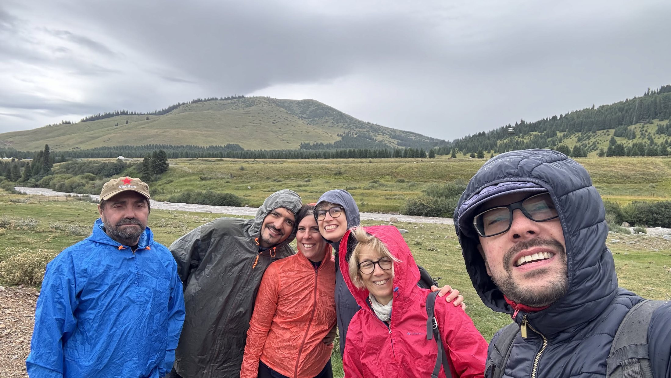 Selfie di gruppo sotto i cappucci, con la pioggia in arrivo e la valle alle spalle