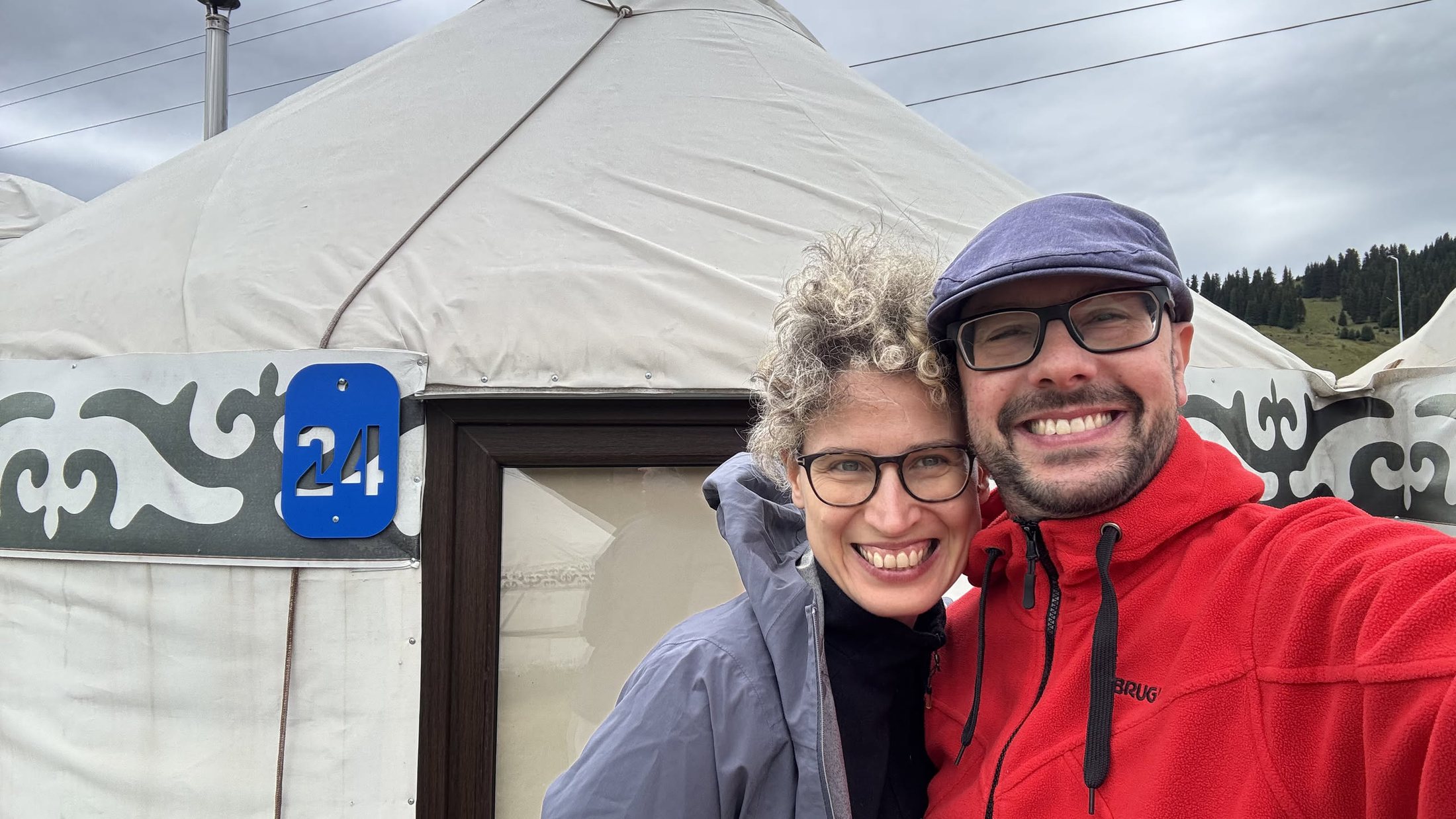 Noi due davanti alla yurta numero 24, con la targa blu sulla porta e le montagne dietro