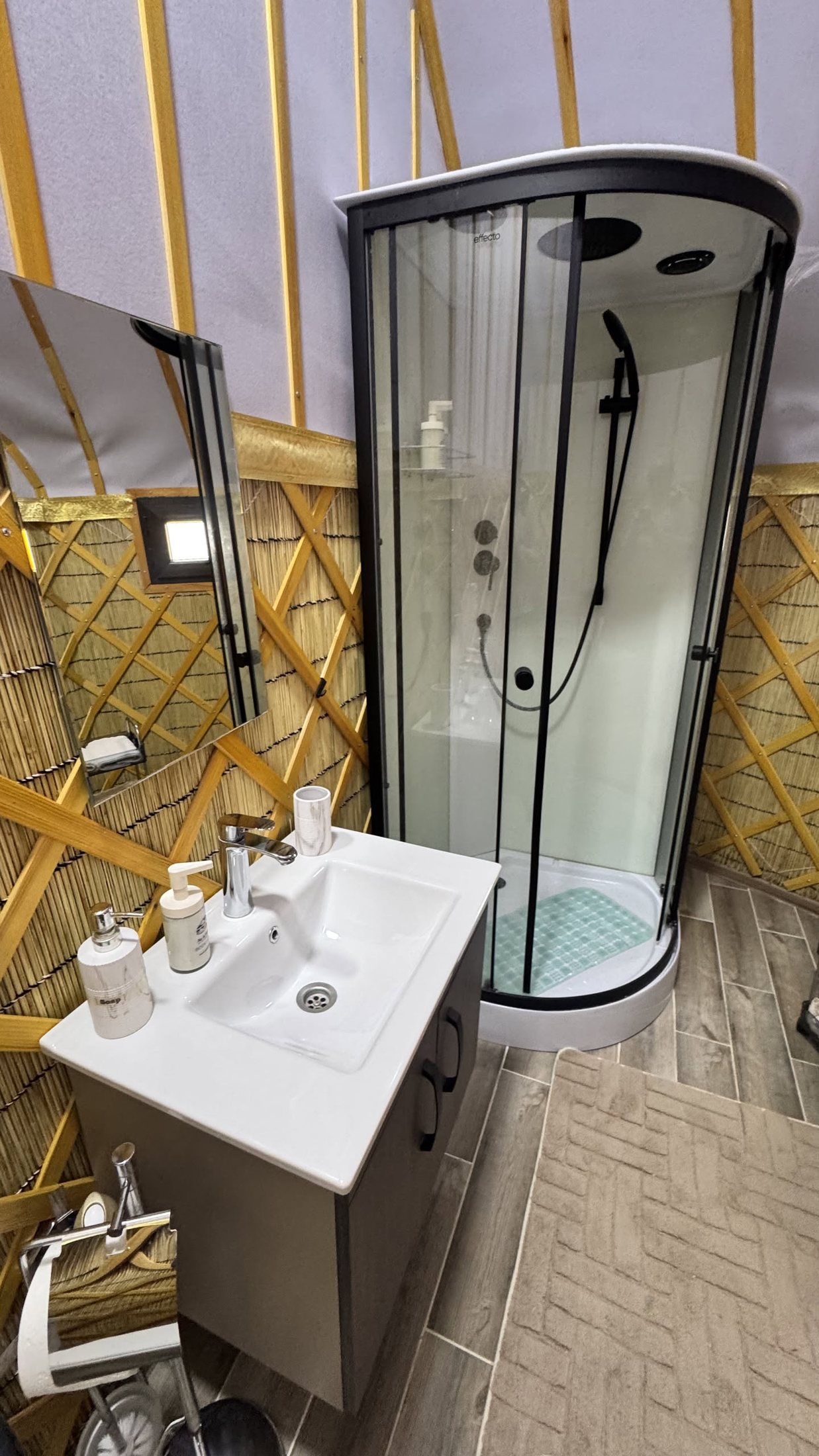 Il bagno dentro la yurta: lavandino e cabina doccia in cristallo appoggiati al graticcio di legno