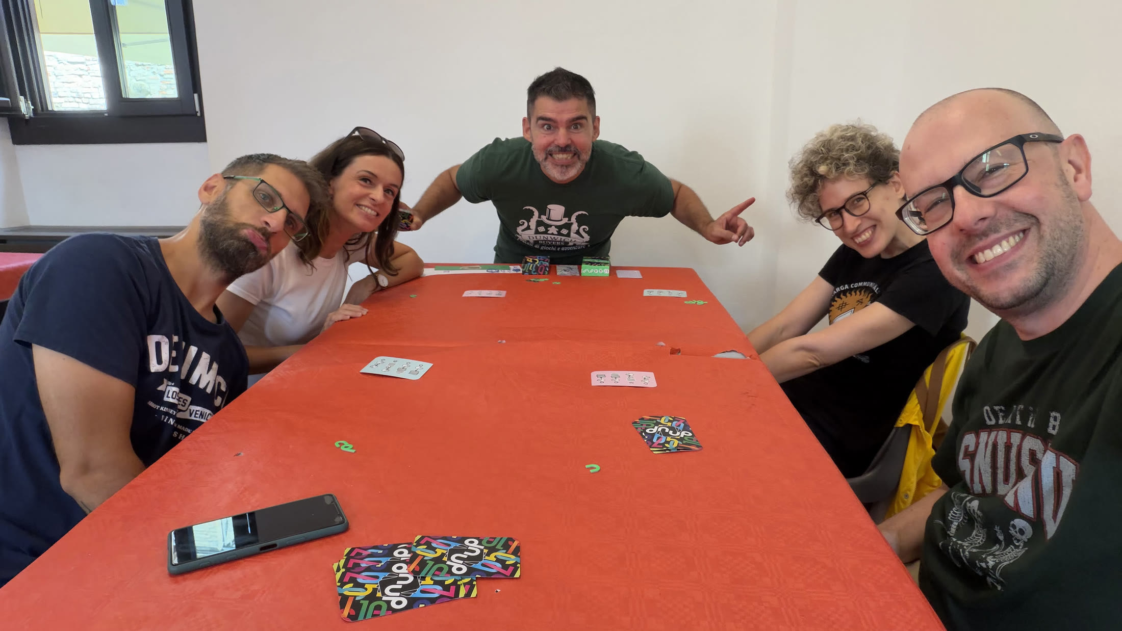 Al tavolo di Gradara Ludens, a metà partita: le carte calate sulla tovaglia rossa e la scatola di DNUP in primo piano.