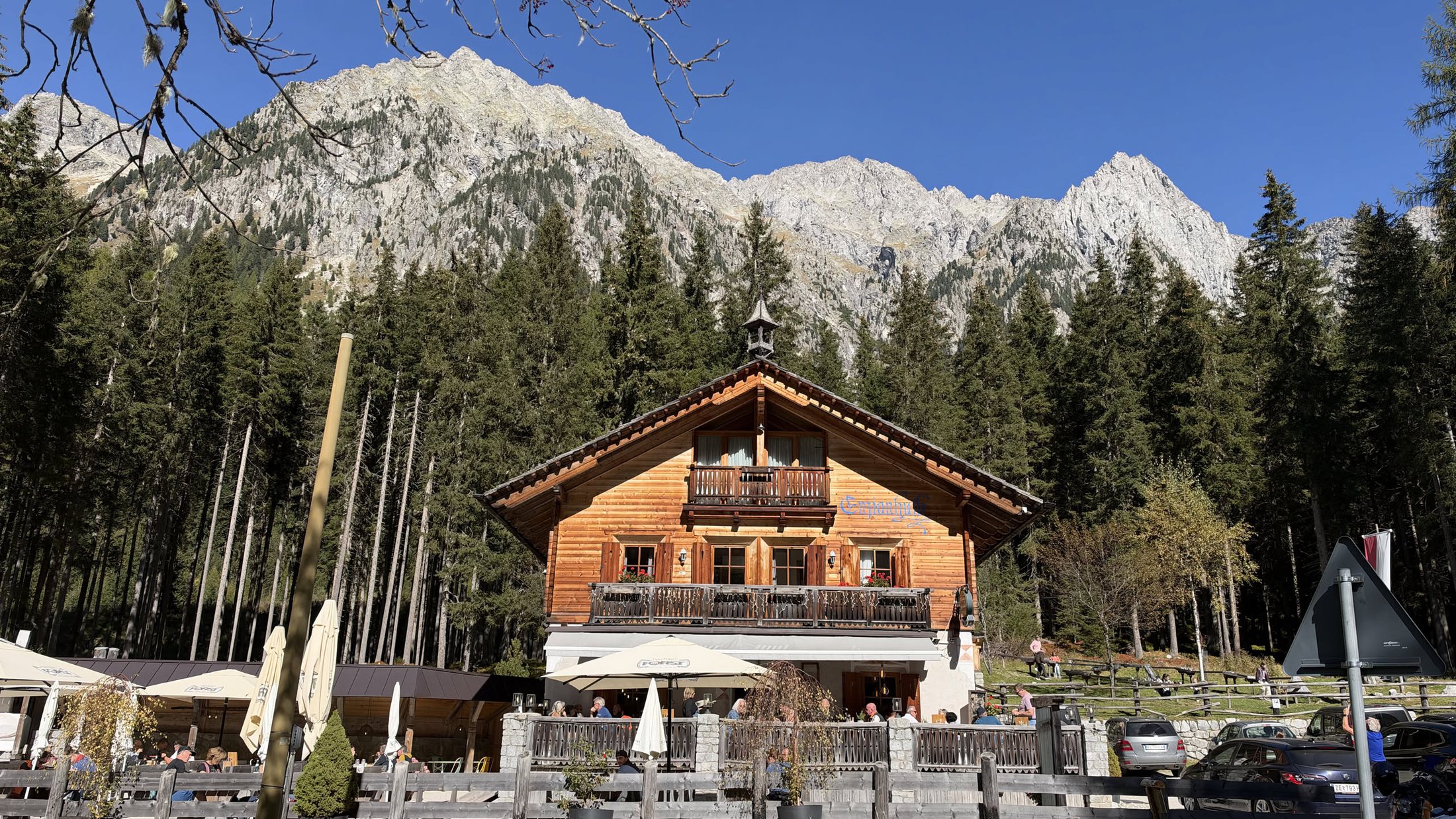 L'Enzianhütte a mezzogiorno: la casa di legno, i balconi, e dietro le creste chiare della valle