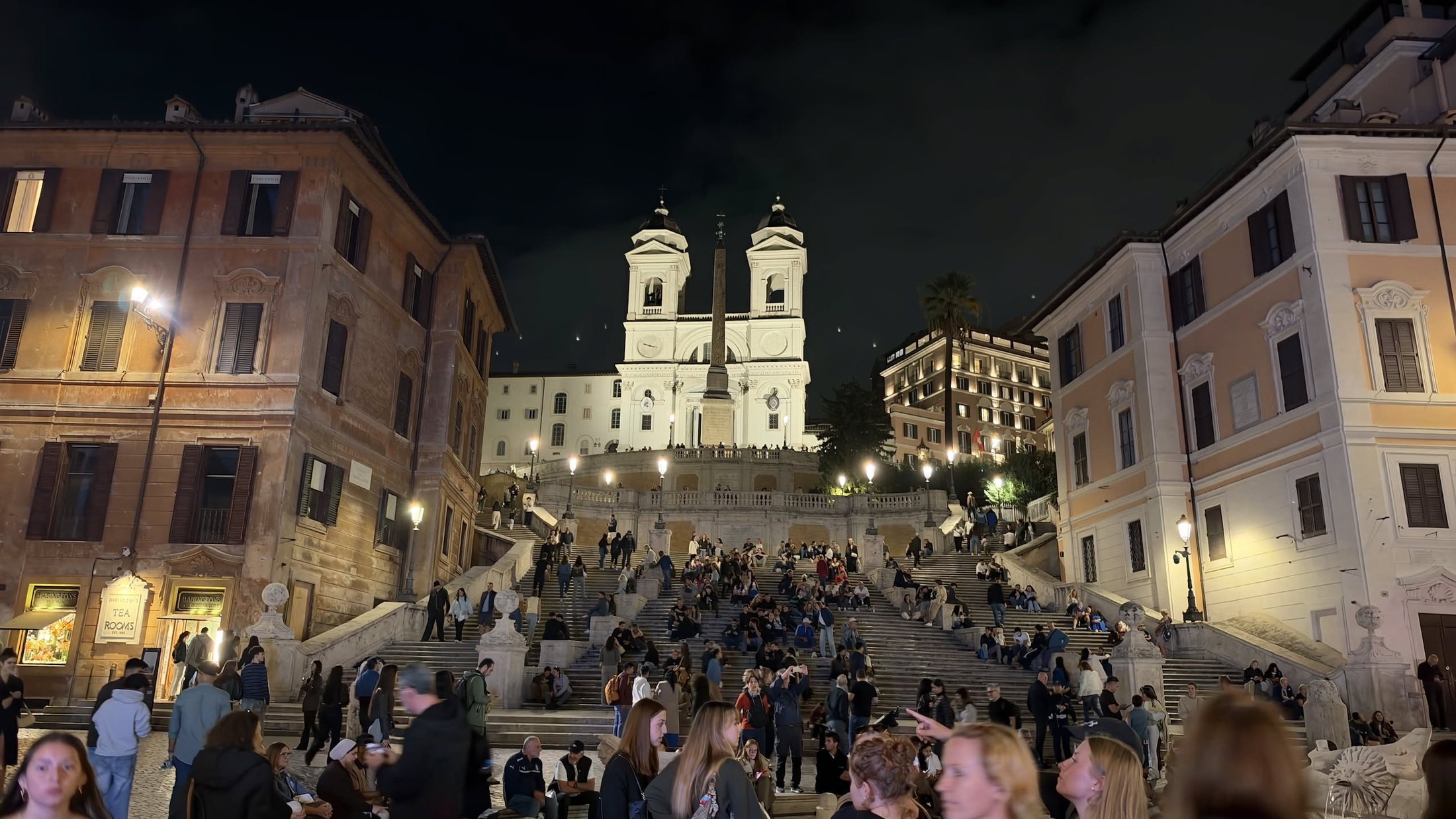 Piazza di Spagna di sera: la scalinata piena e Trinità dei Monti illuminata.